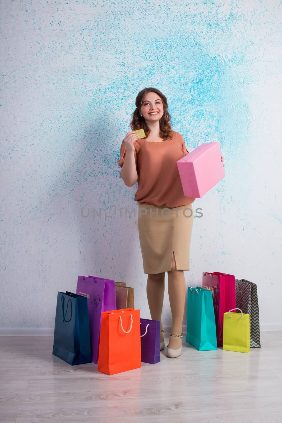 Happy smiling woman after shopping stands with colourful paper bags, boxes showing banking credit card