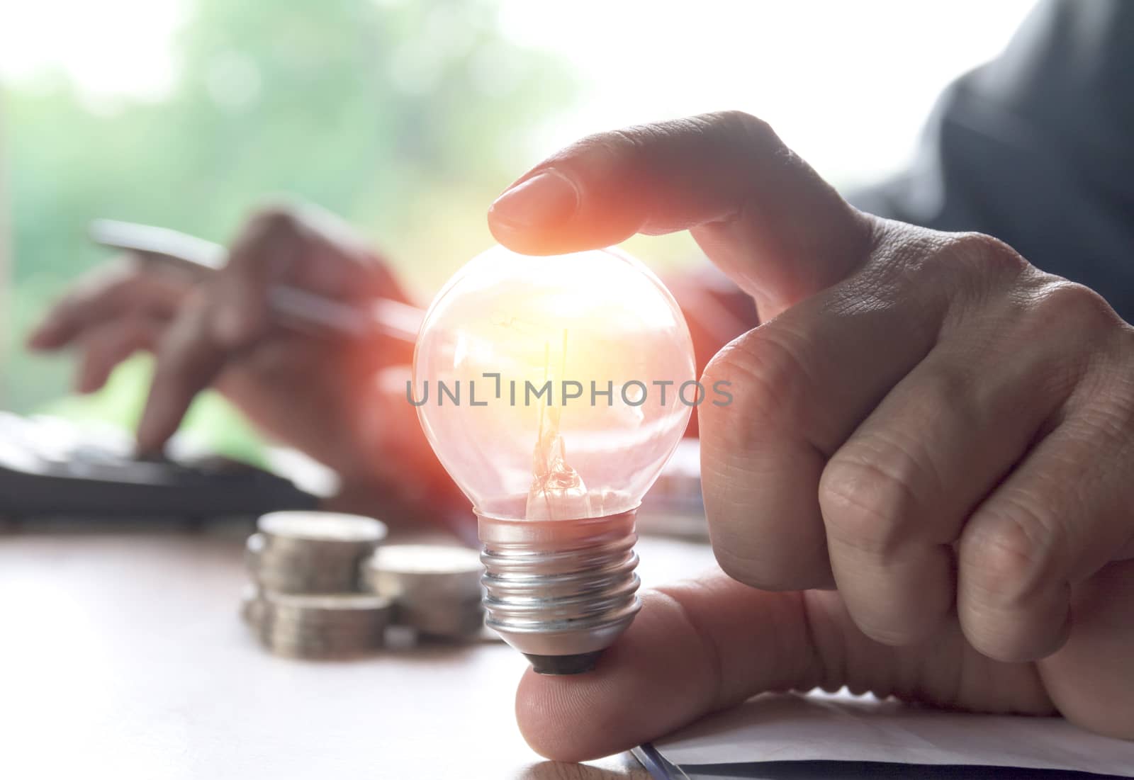 Hand holding light bulbs glowing and using calculator. Idea, creativity and saving energy with light bulbs concept.
