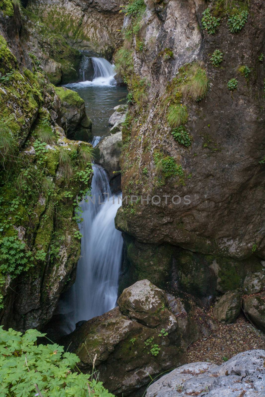 A natural waterfall between beautiful rocks covered with green moss.