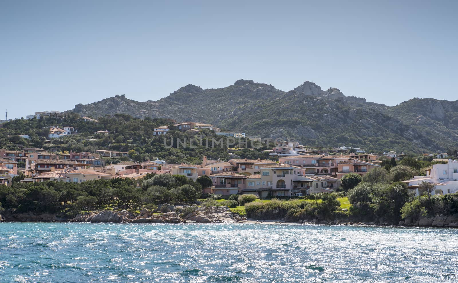skyline of ht exclusive village of porto servo on sradinia island italy with the mountains as background and the blue water in the sea as foreground.