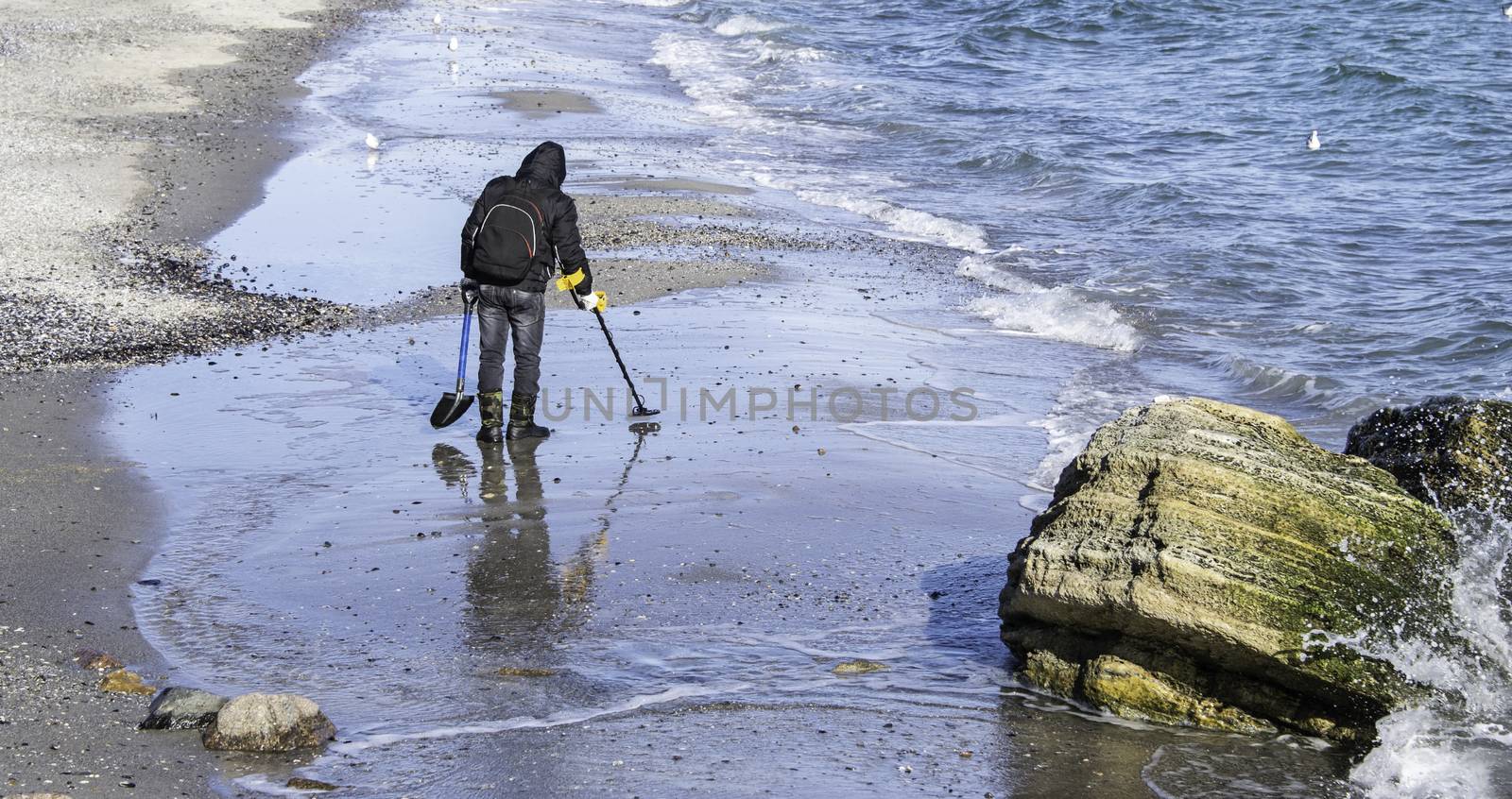 ODESSA, UKRAINE - 01.25.2017. Man with metal detector looking for treasure on the beach in a early winter morning.