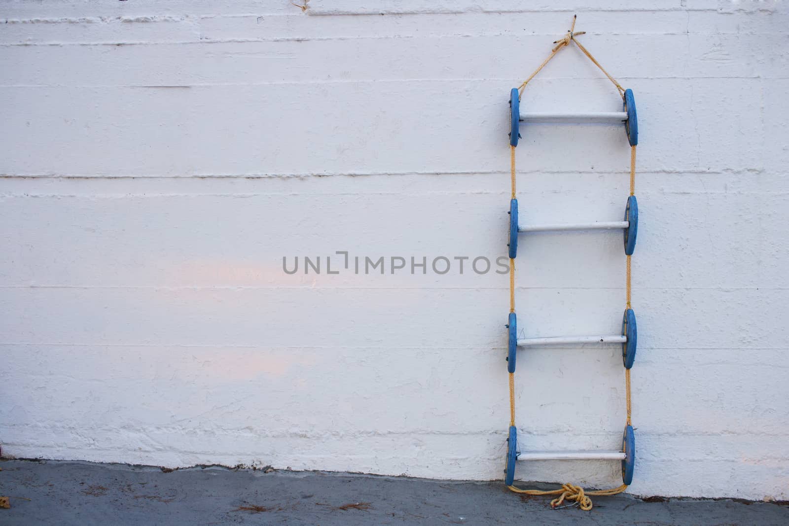 Conceptional geometrical composition of blue marine ladder leaning against vertical white painted wall