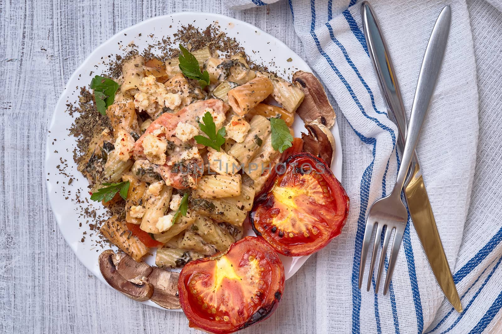 Paste from macaroni with vegetables, with tomatoes and seasoned with a basil. It is decorated with parsley. On a light background with ordinary devices.