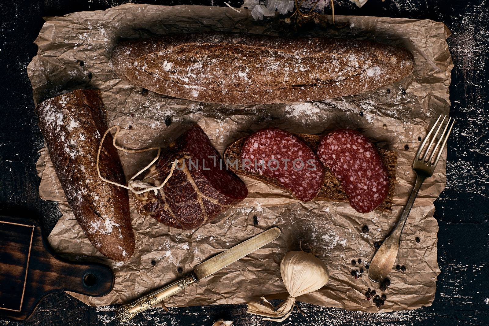 raw smoked sausage with rye bread and garlic on parchment paper with elements of kitchen utensils in in style a rustic