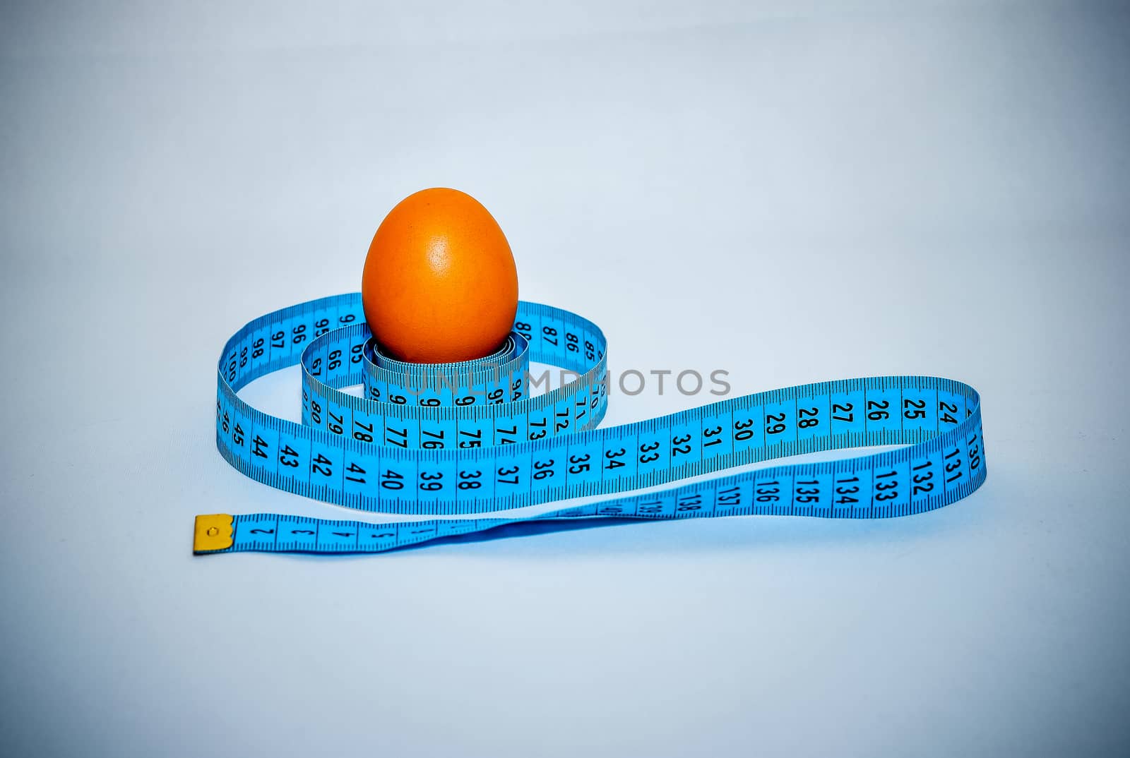 Egg wrapped in blue measuring tape, slimming concept.