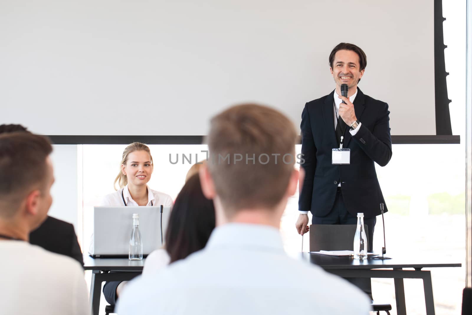 Speaker at business conference near white screen and audience