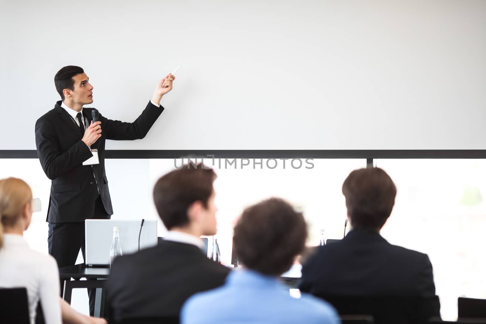 Speaker at business conference near white screen and audience