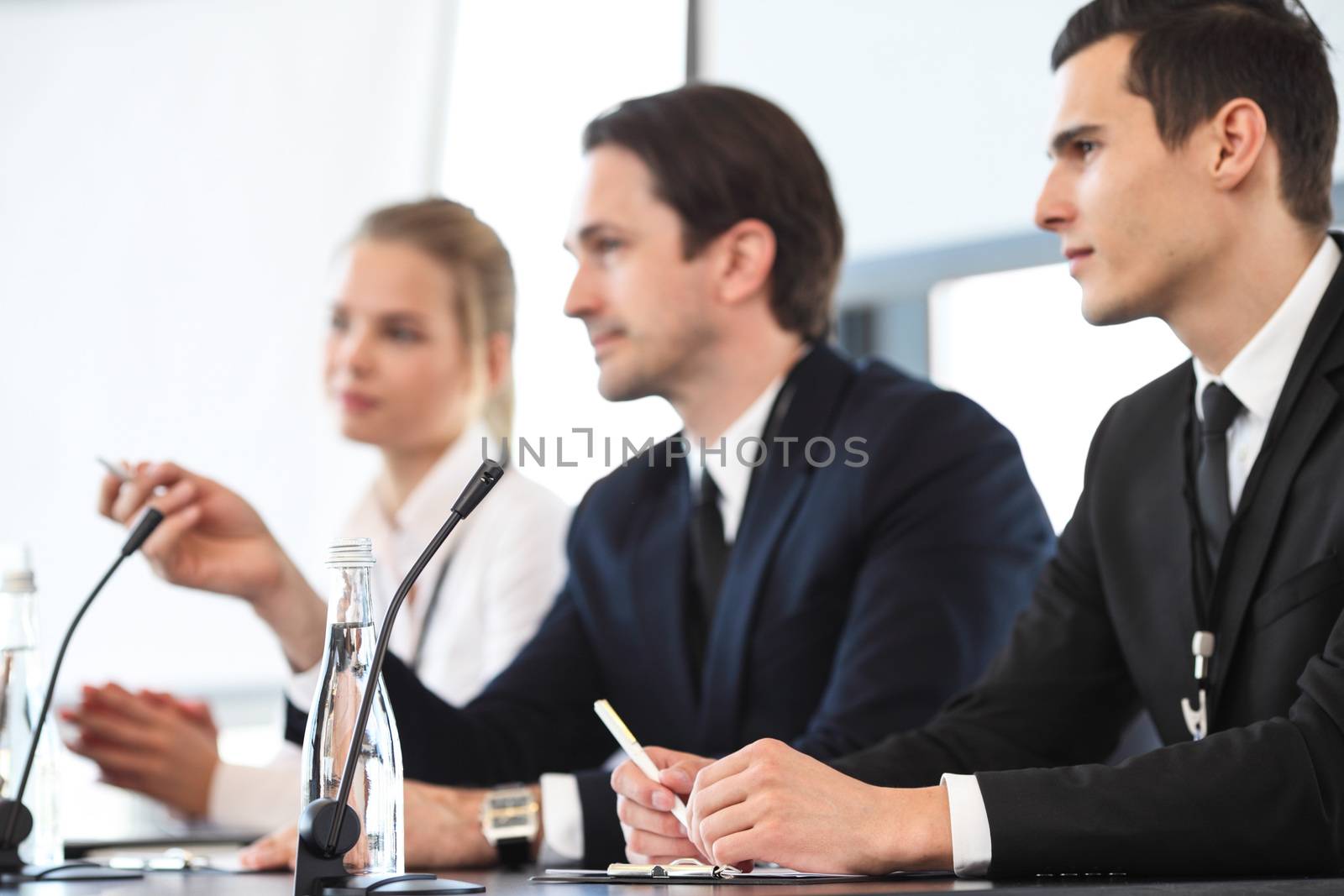 Group of speakers at business meeting at the table with microphones