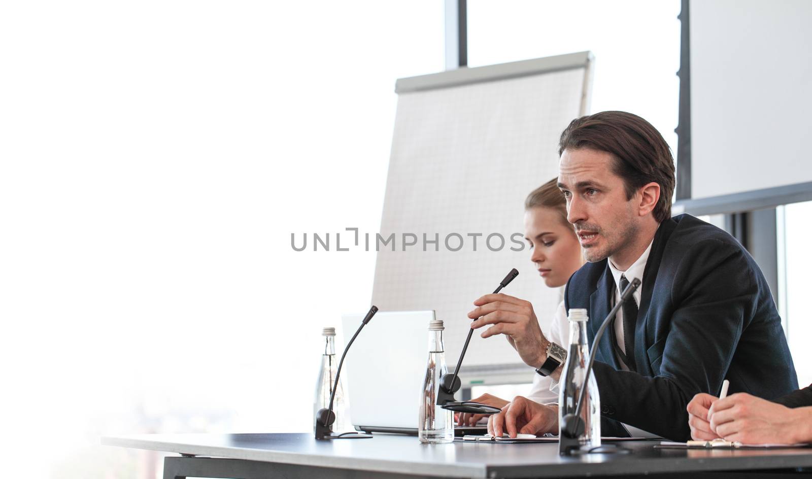 Group of speakers at business meeting at the table with microphones