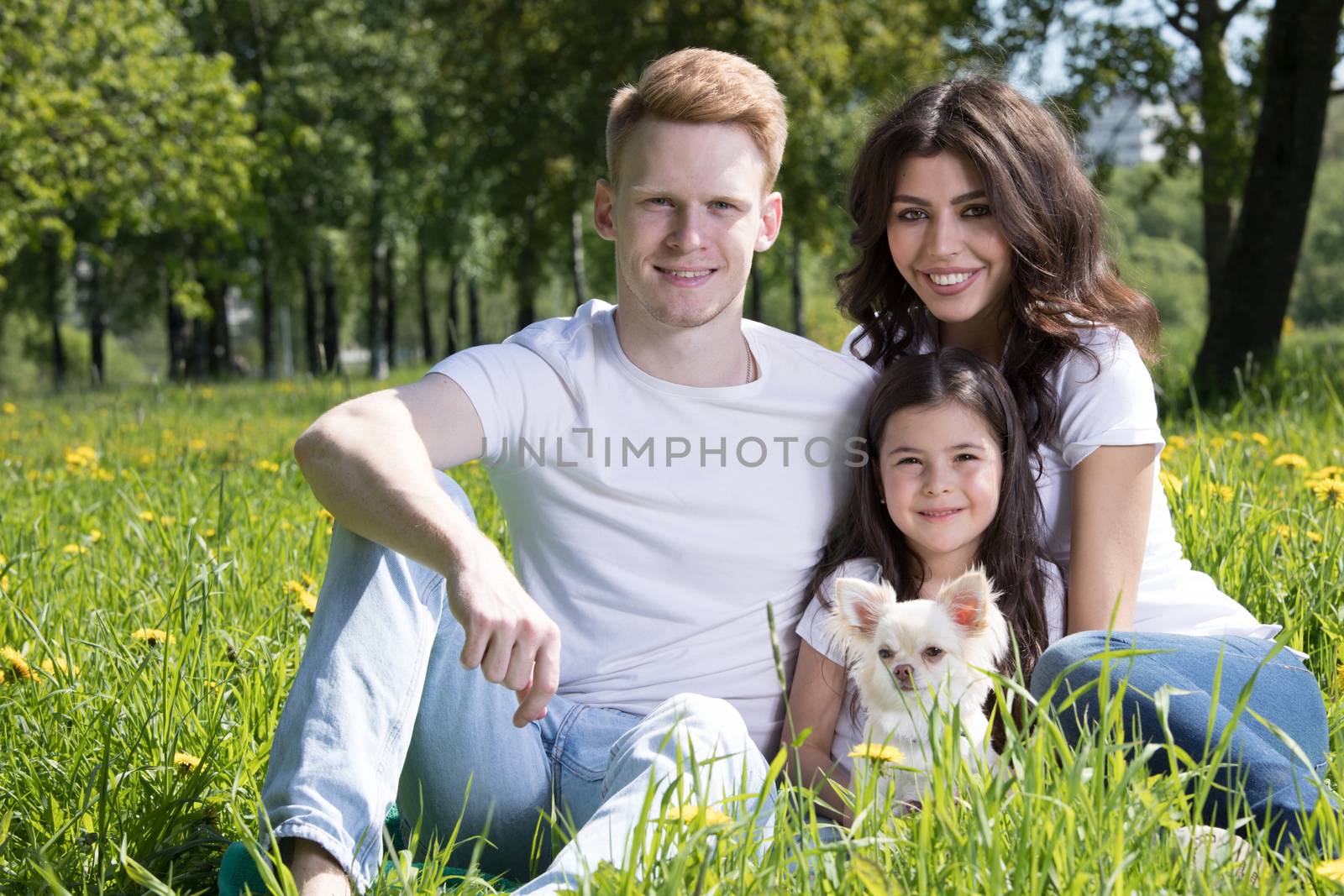 Happy family with man, woman and child sitting on grass in city park