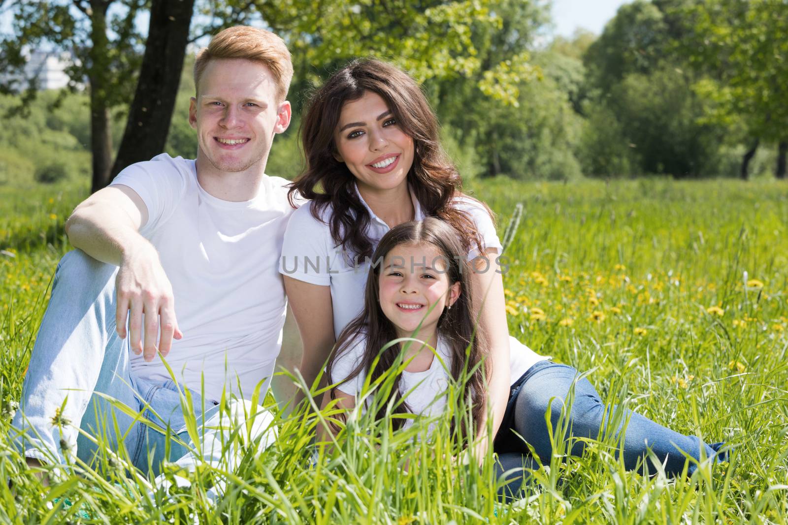 Happy family with man, woman and child sitting on grass in city park