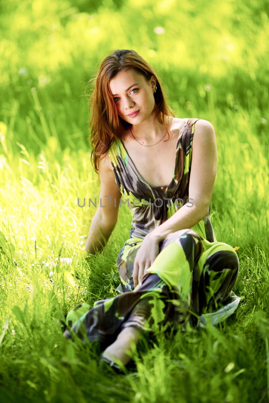 Beautiful woman sitting in a green field enjoying the summer sunlight