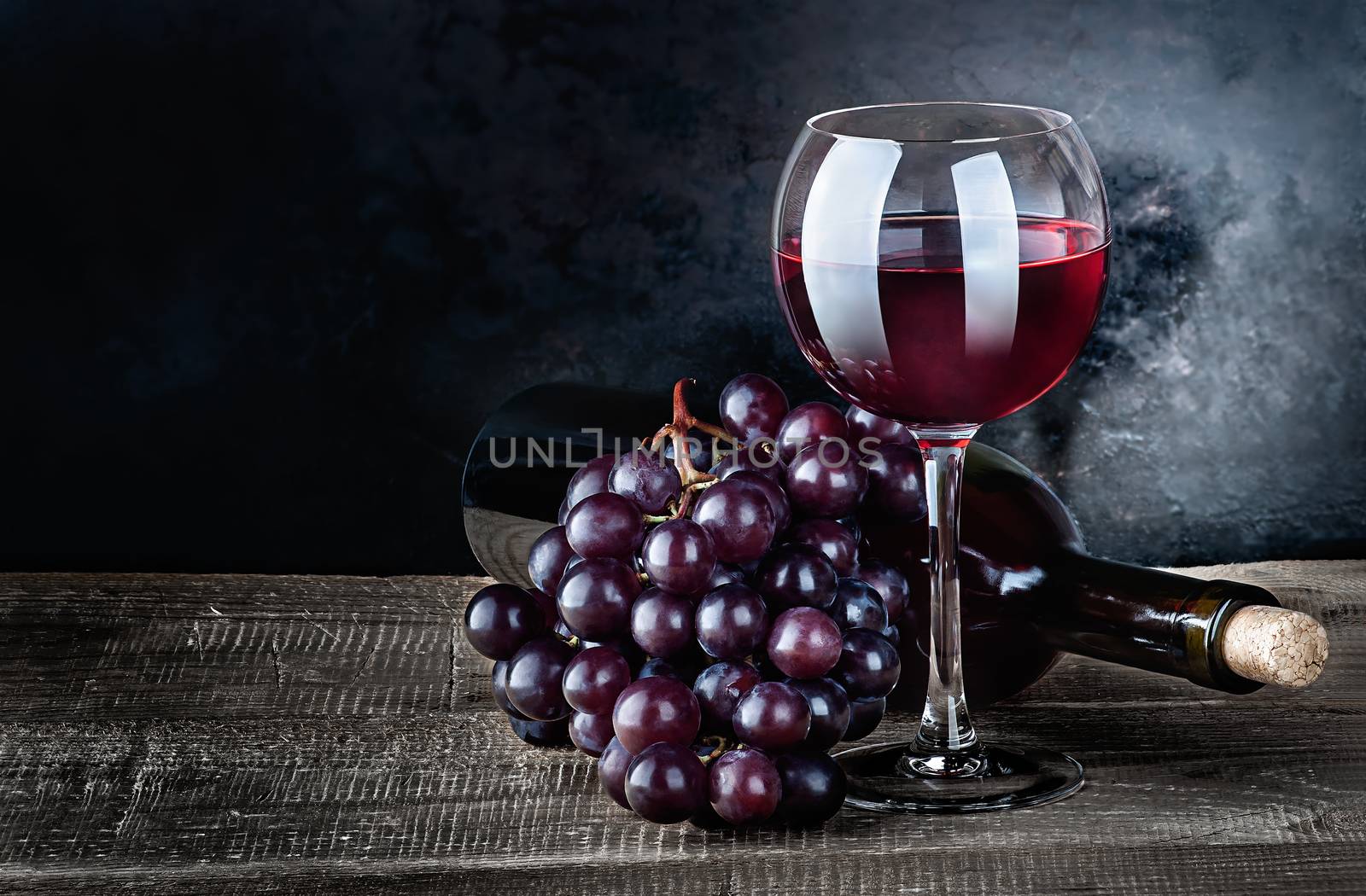 Red wine with grapes and bottle on a wooden table. The bottle lies. Dark background.