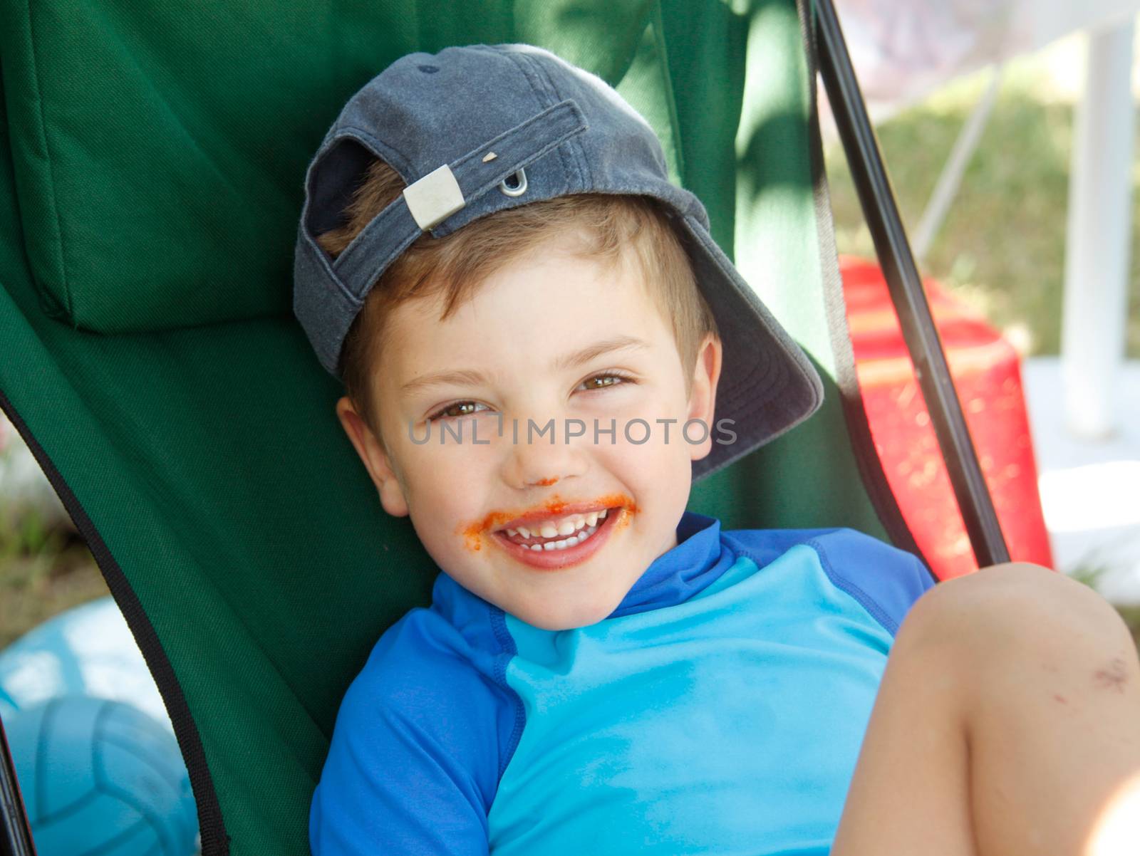 Portrait of a smiling little boy with red sauce around his mouth.