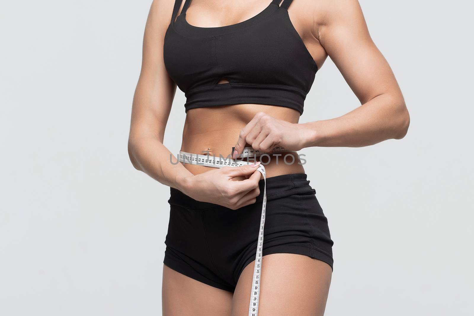 Bodybuilder girl measures the waist measuring tape on a gray background