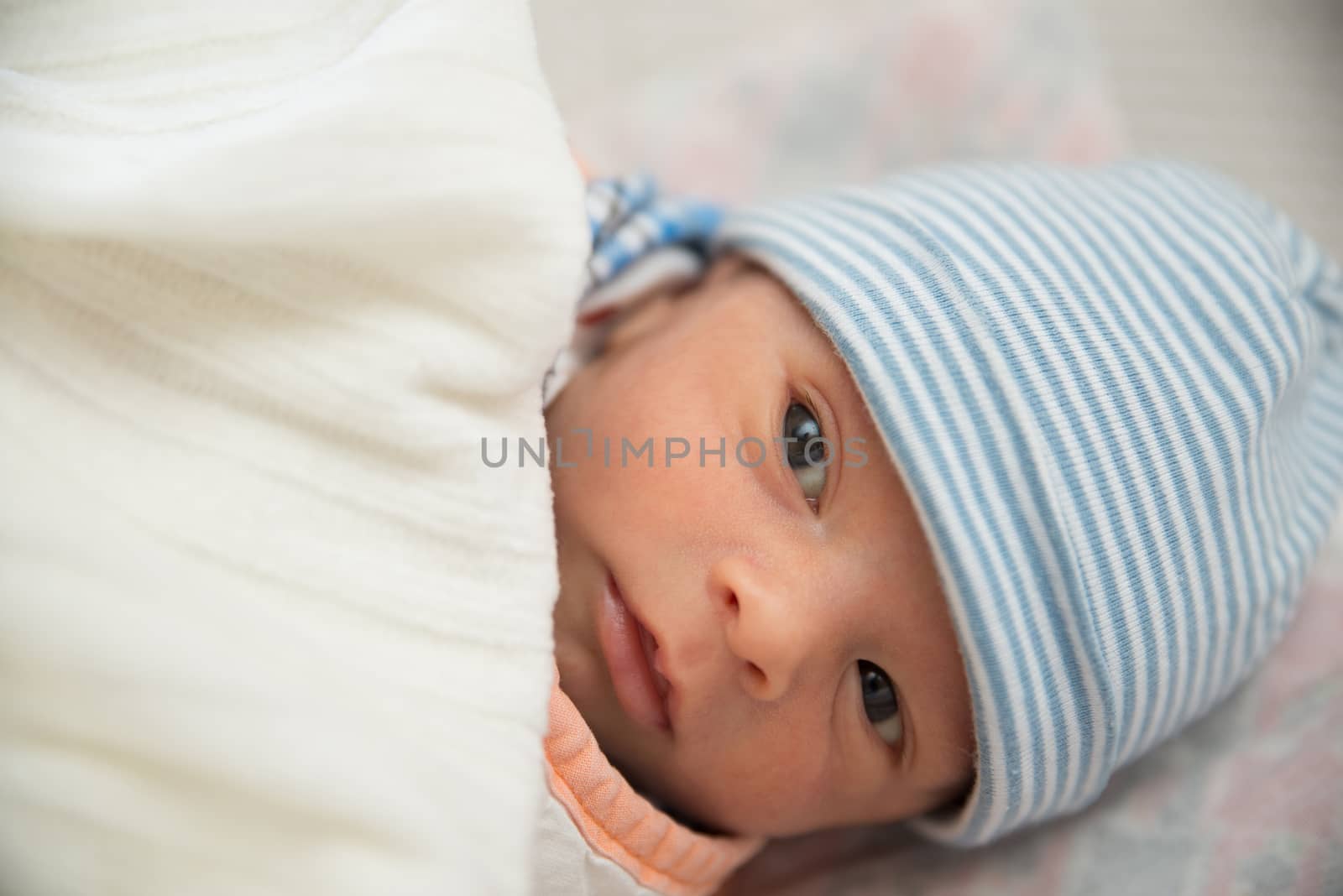 Cute Eurasian newborn baby boy lying on bed and wearing a striped cap