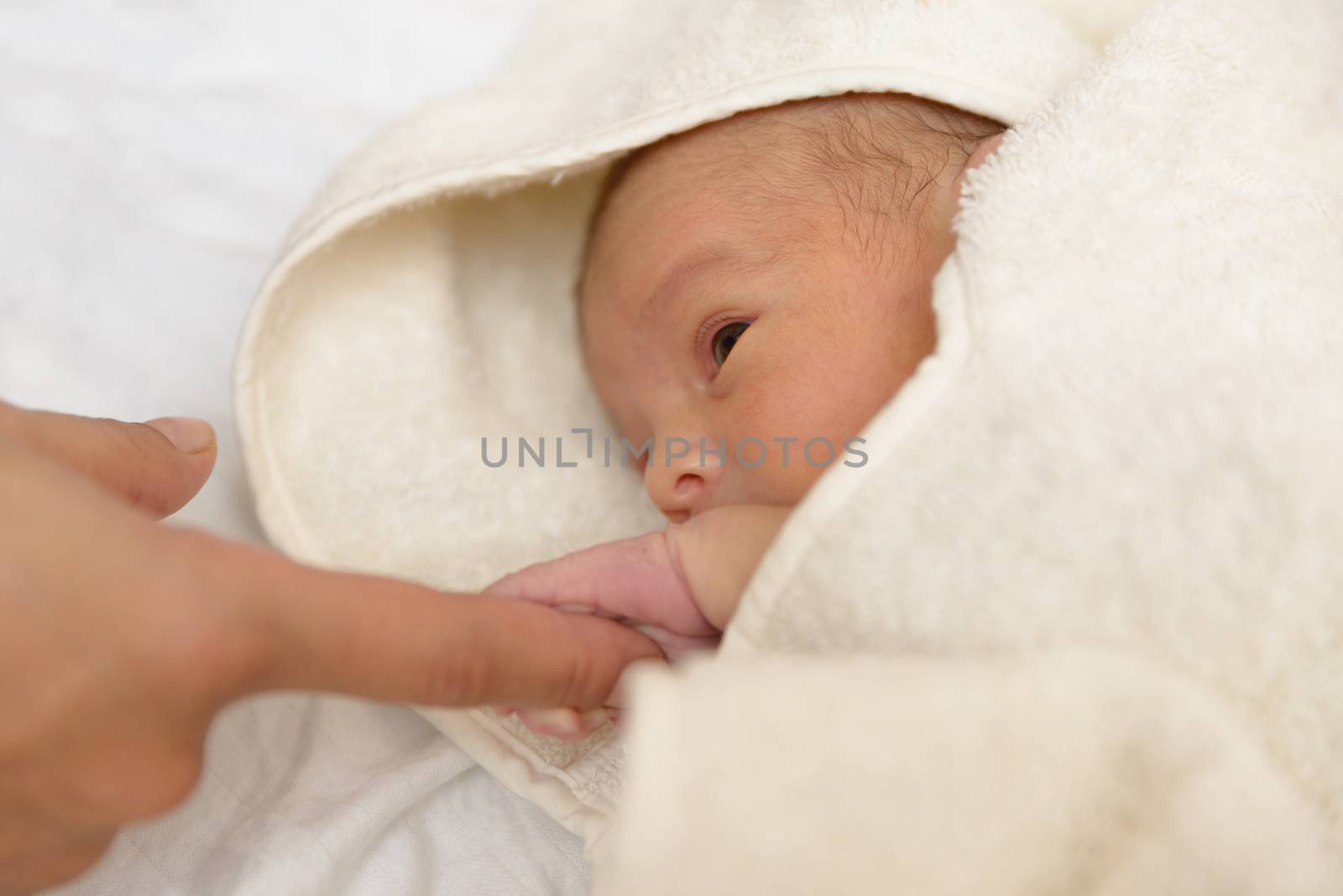 Newborn baby boy in a towel after the bath and holding his mother's finger