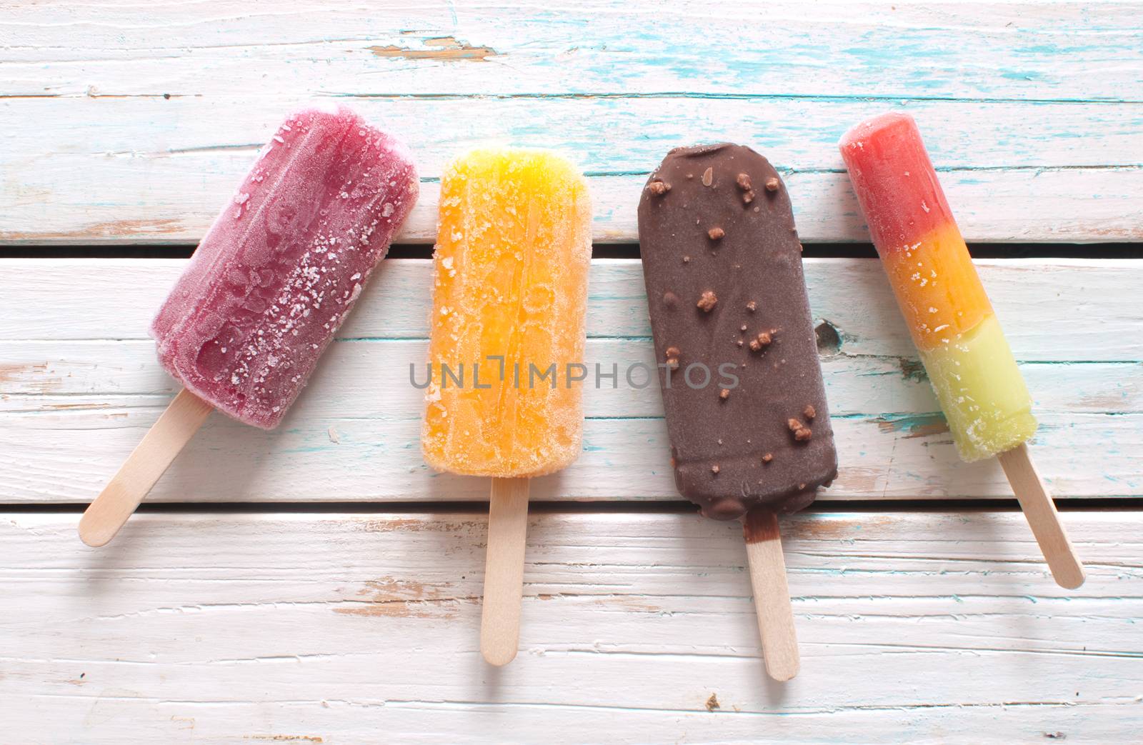 Various flavored ice popsicles over wooden background