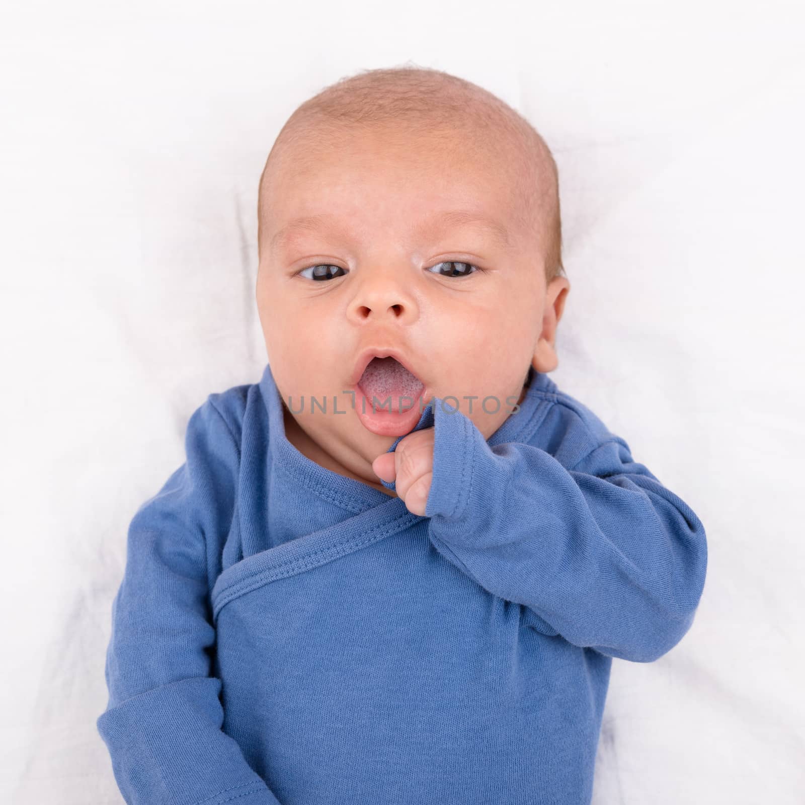 Cute eurasian newborn baby boy wearing a blue infant bodysuit on white sheet