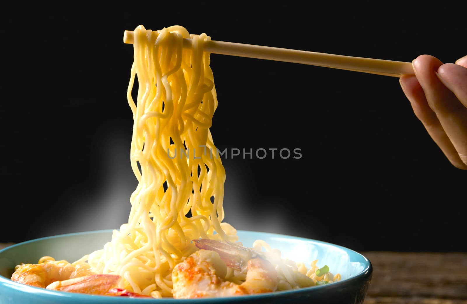 Hand using chopsticks pickup instant noodles with smokes isolated on black background.