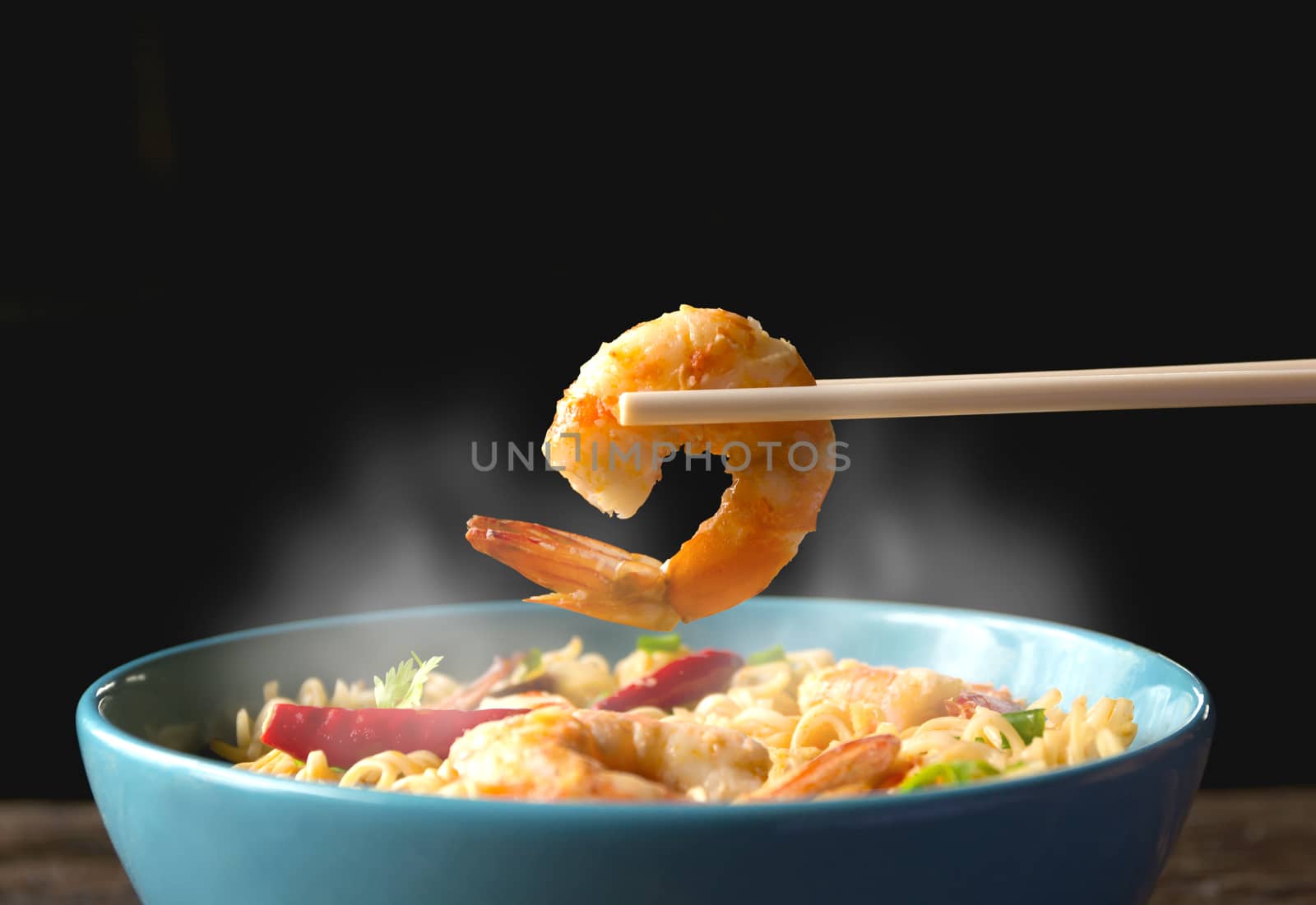Hand using chopsticks pickup shrimp with instant noodles with smokes isolated on black background.