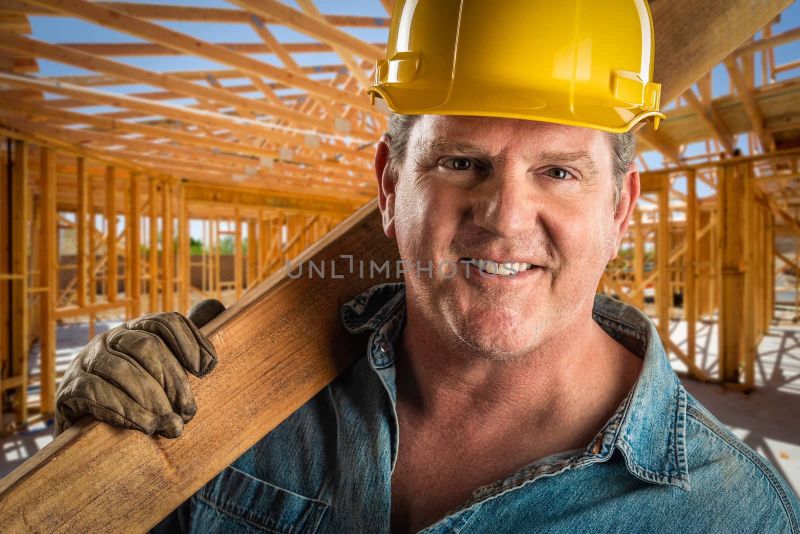 Serious Contractor in Hard Hat Carrying Wood Plank At Construction Site. by Feverpitched