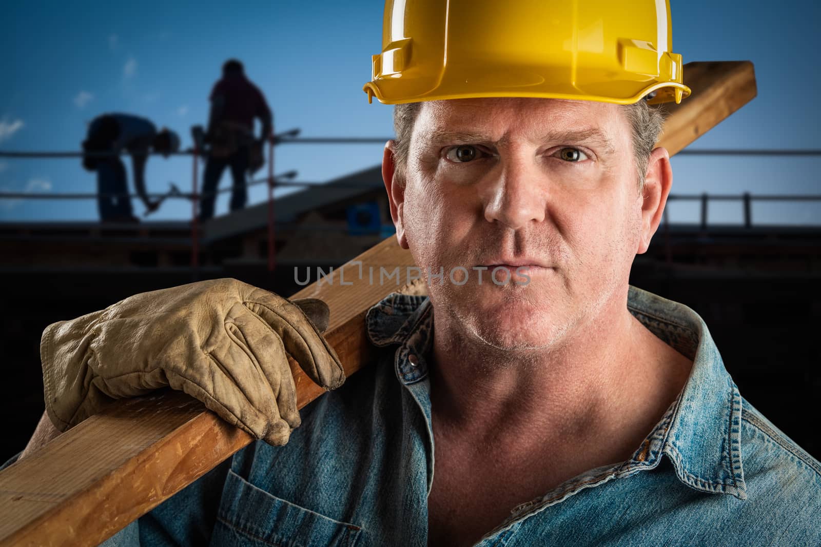 Serious Contractor in Hard Hat Carrying Wood Plank At Construction Site. by Feverpitched