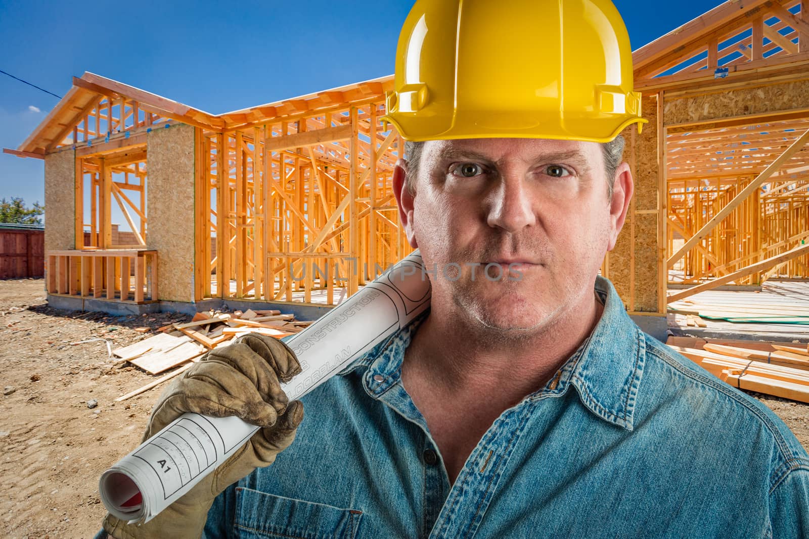 Serious Contractor in Hard Hat Holding Floor Plans At Construction Site.