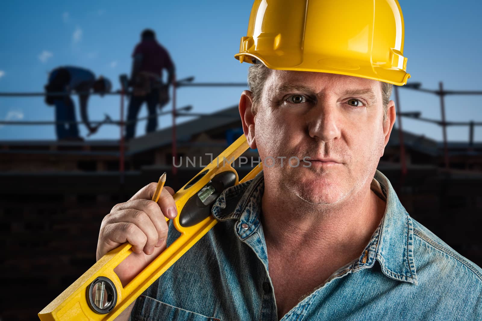 Serious Contractor in Hard Hat Holding Level and Pencil At Construction Site. by Feverpitched