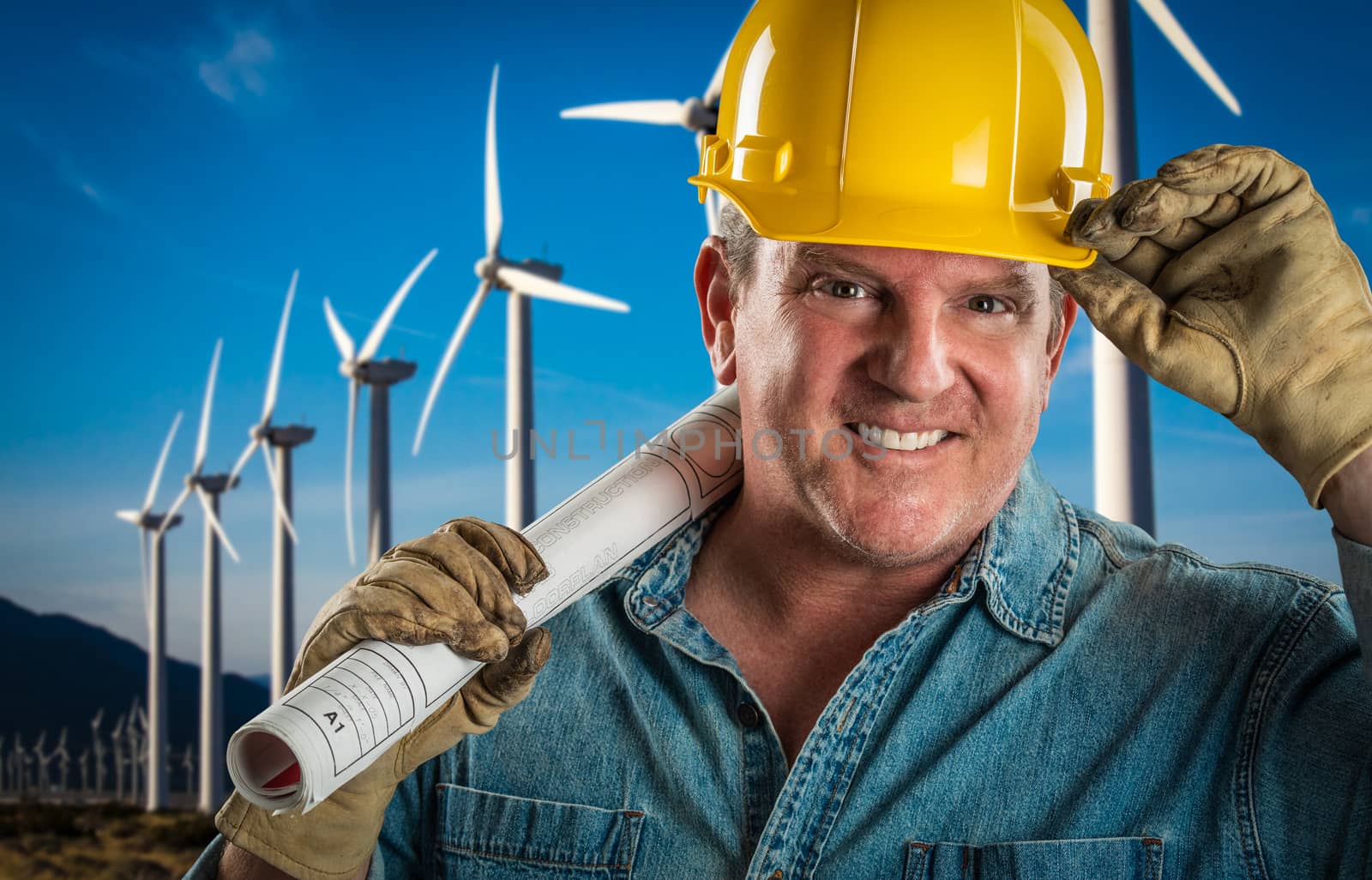 Smiling Contractor in Hard Hat Holding Extention Cord Outdoors Near Wind Turbines. by Feverpitched