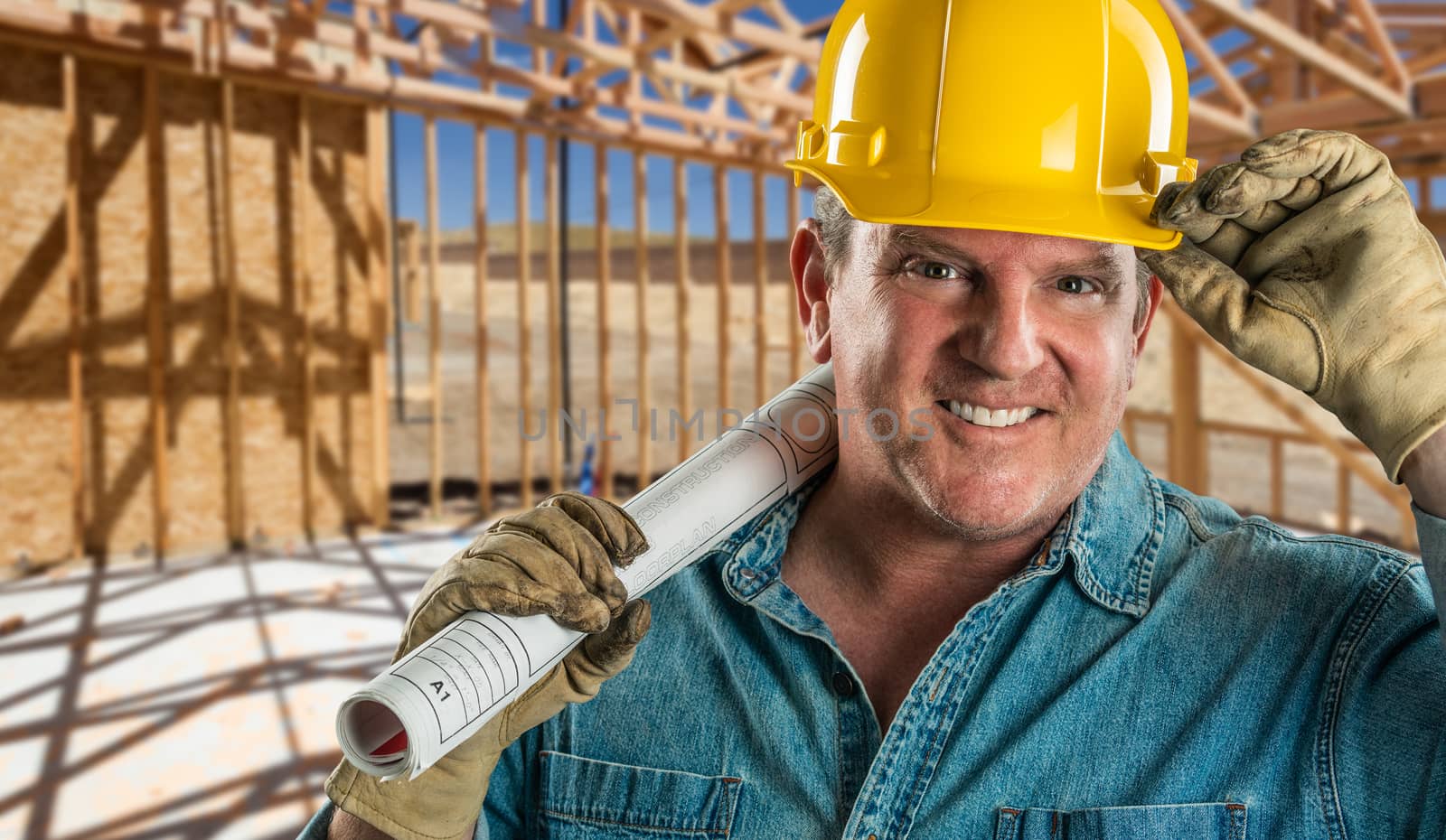 Smiling Contractor in Hard Hat Holding Floor Plans At Construction Site. by Feverpitched