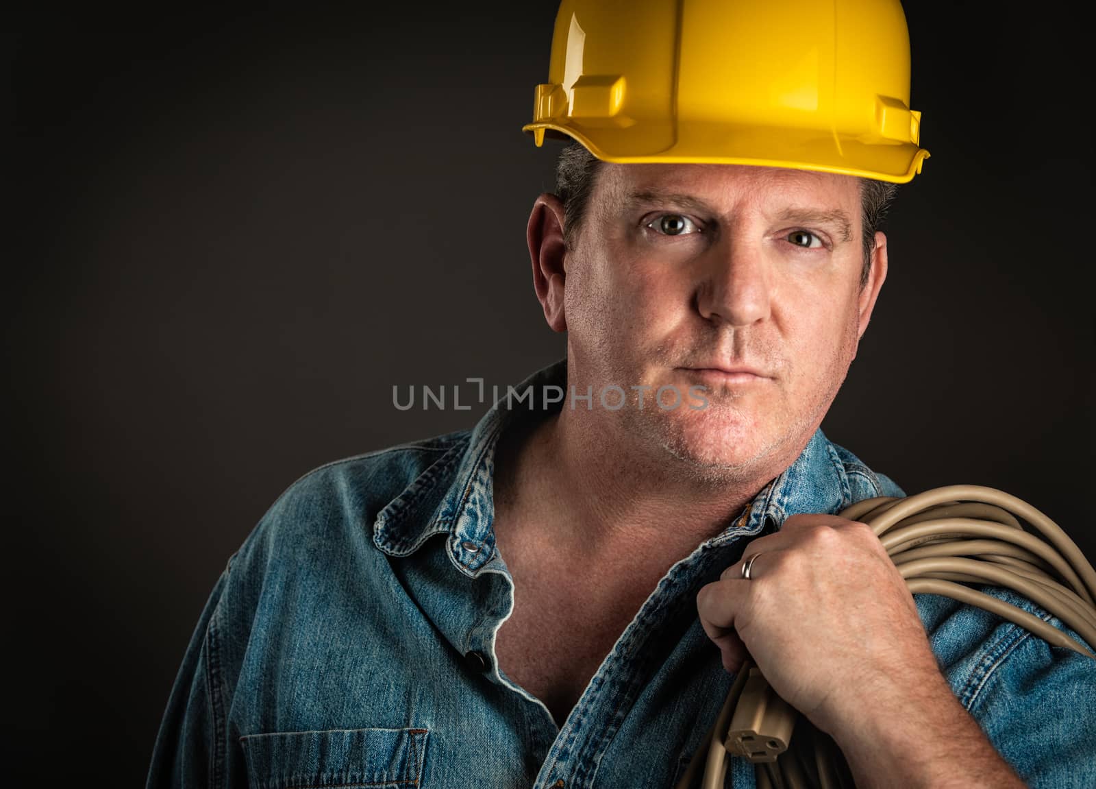 Serious Contractor in Hard Hat Holding Extention Cord With Dramatic Lighting.