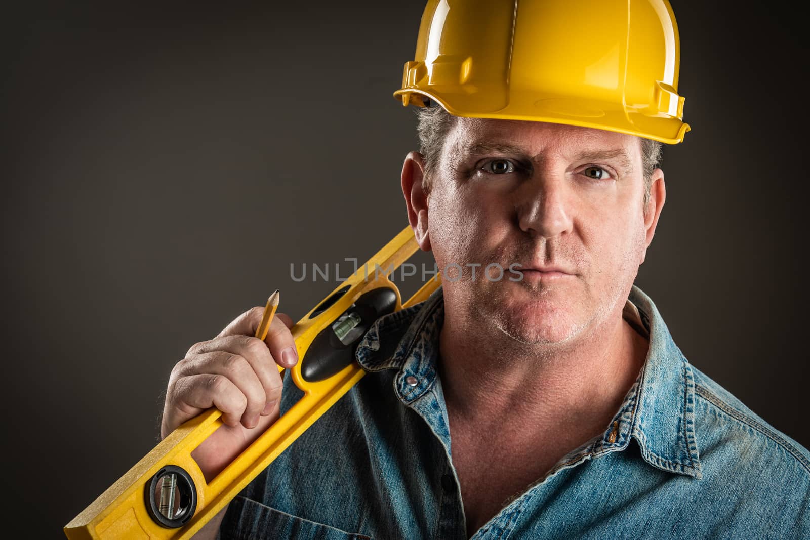 Serious Contractor in Hard Hat Holding Level and Pencil With Dramatic Lighting. by Feverpitched