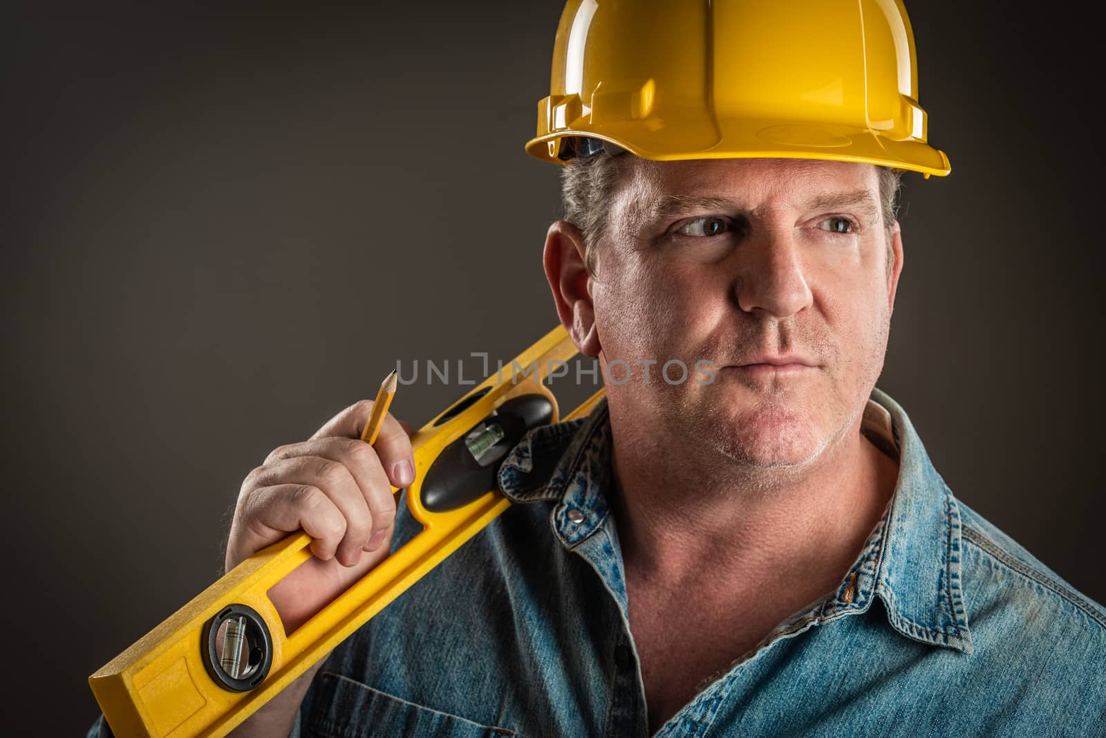 Serious Contractor in Hard Hat Holding Level and Pencil With Dramatic Lighting. by Feverpitched