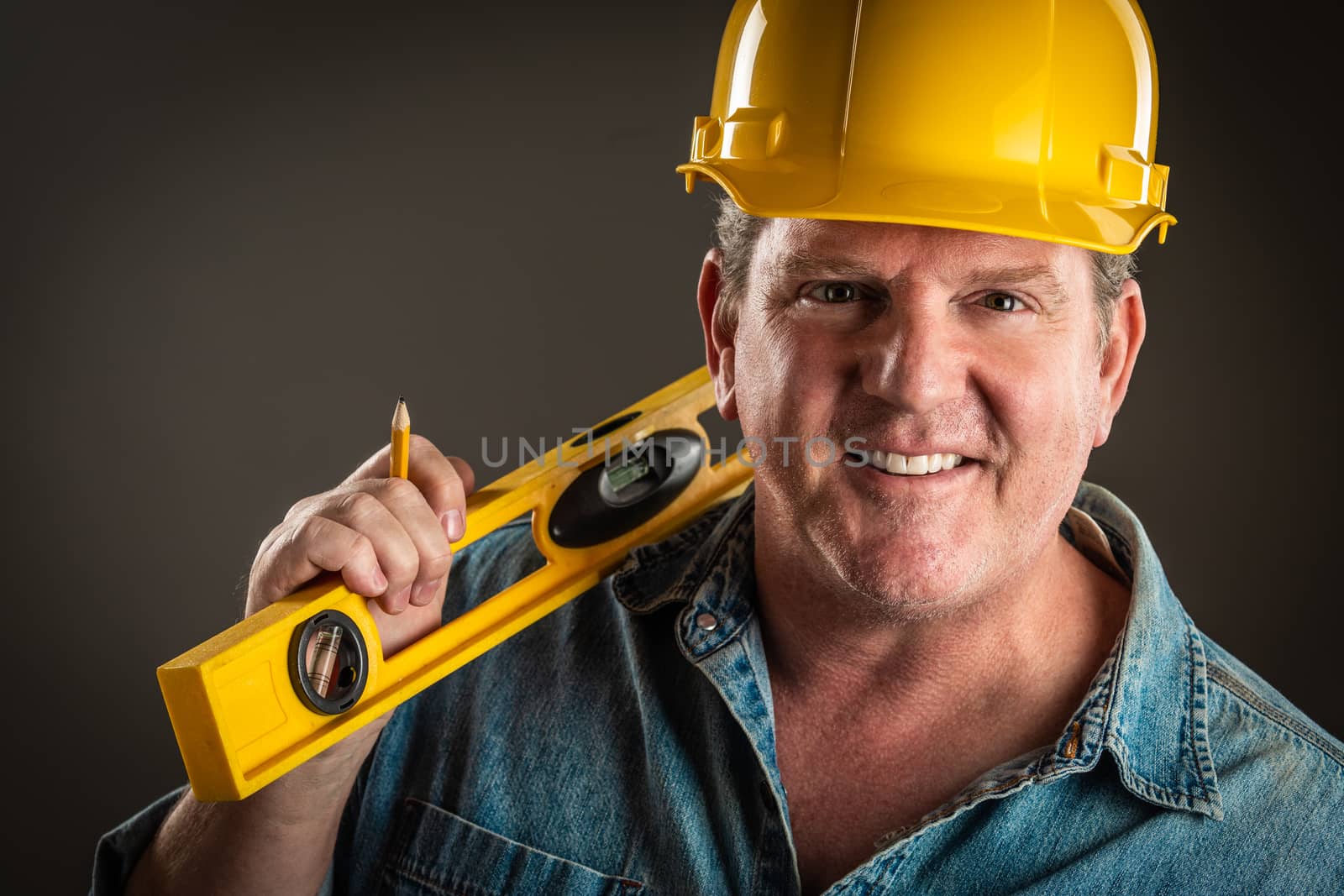 Smiling Contractor in Hard Hat Holding Level and Pencil With Dramatic Lighting.