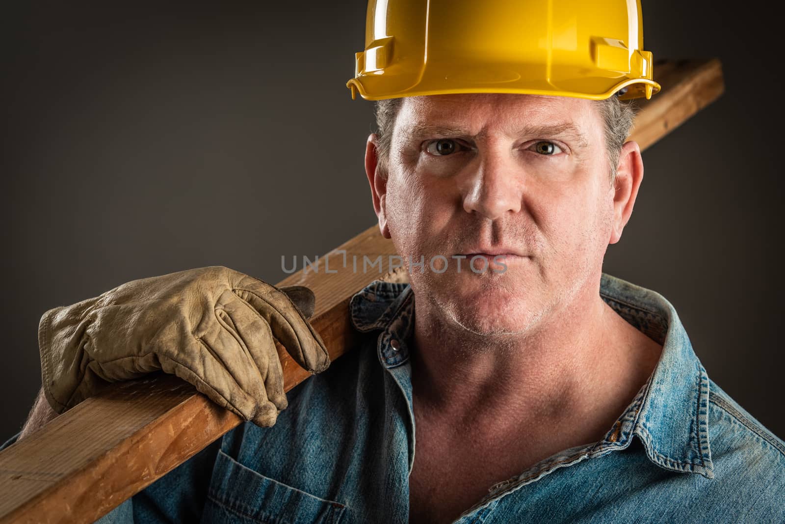 Serious Contractor in Hard Hat Holding Plank of Wood With Dramatic Lighting.