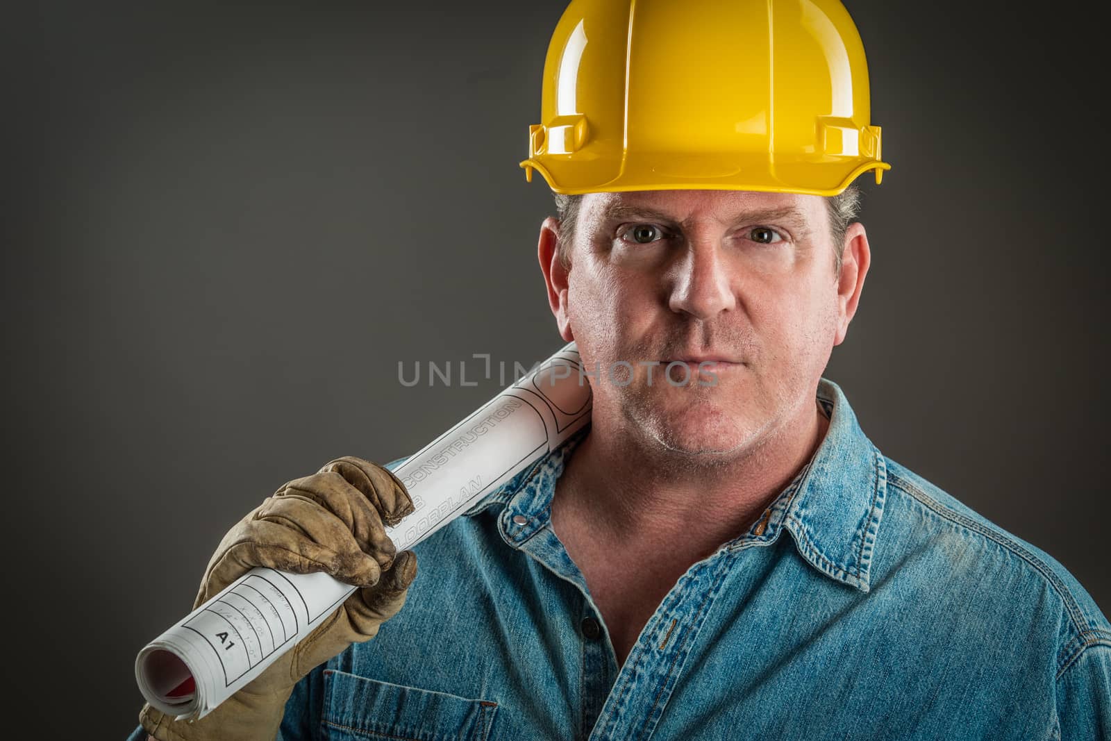 Serious Contractor in Hard Hat Holding Floor Plans With Dramatic by Feverpitched