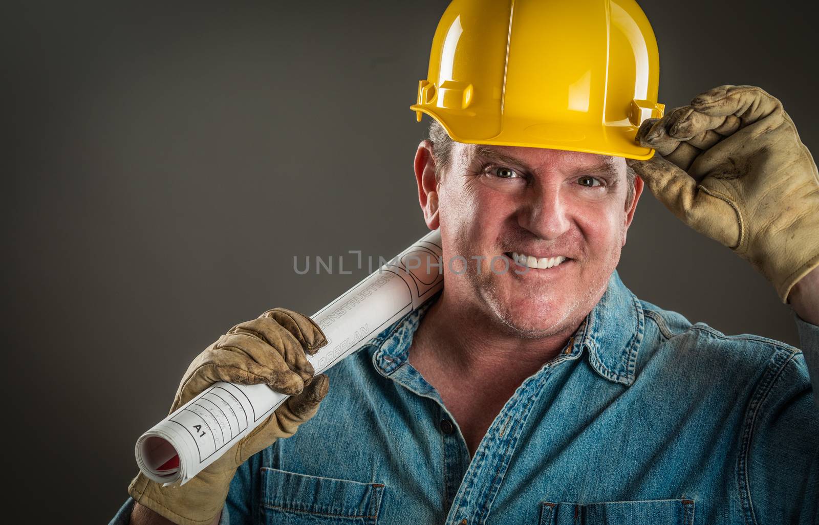 Smiling Contractor in Hard Hat Holding Floor Plans With Dramatic by Feverpitched