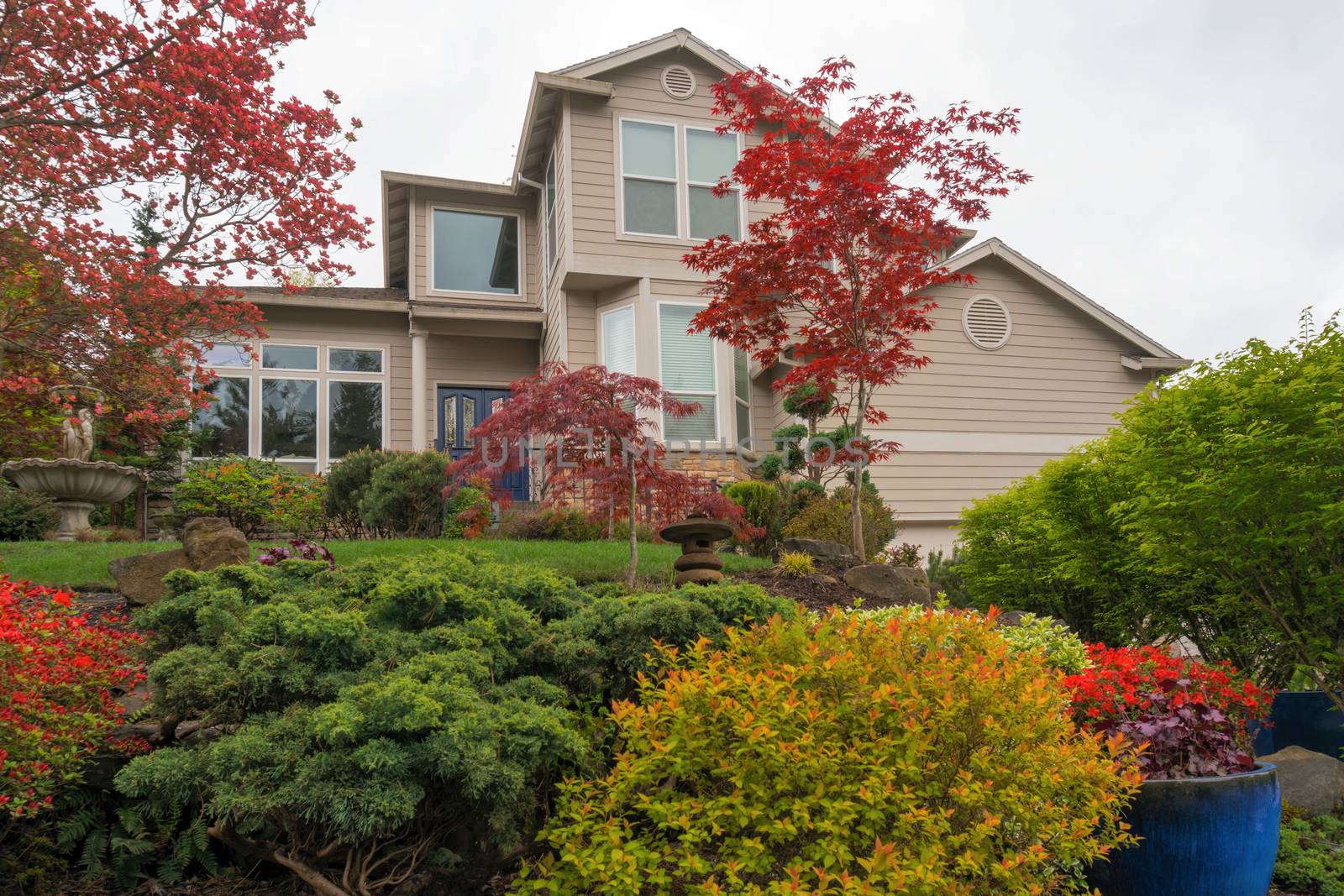 Lush front yard garden landscaping of single family home withwater fountain ceramic pots trees shrubs green grass lawn