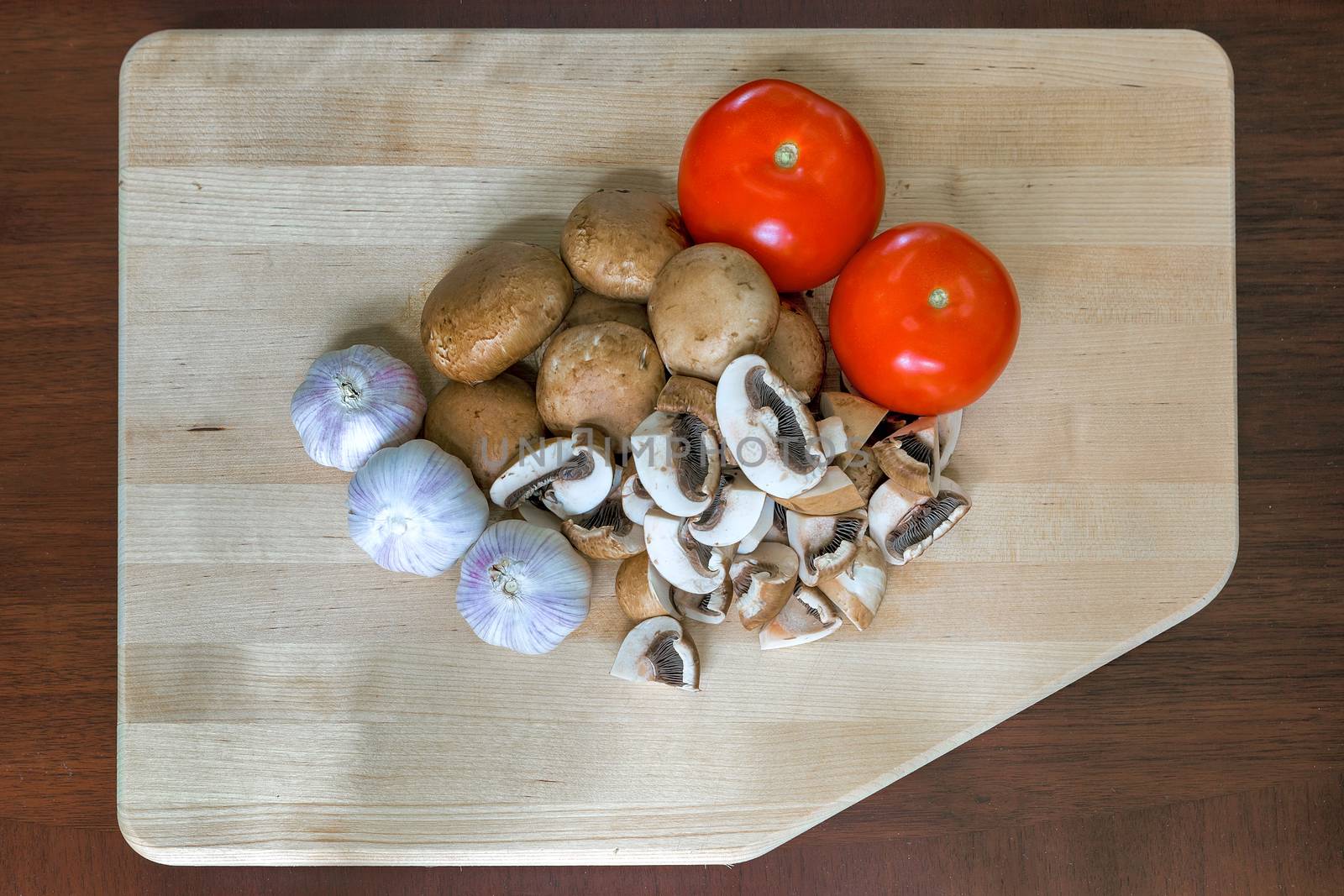 Tomatoes Garlic Cloves Baby Portobello Mushrooms on Kitchen Cutting Board closeup