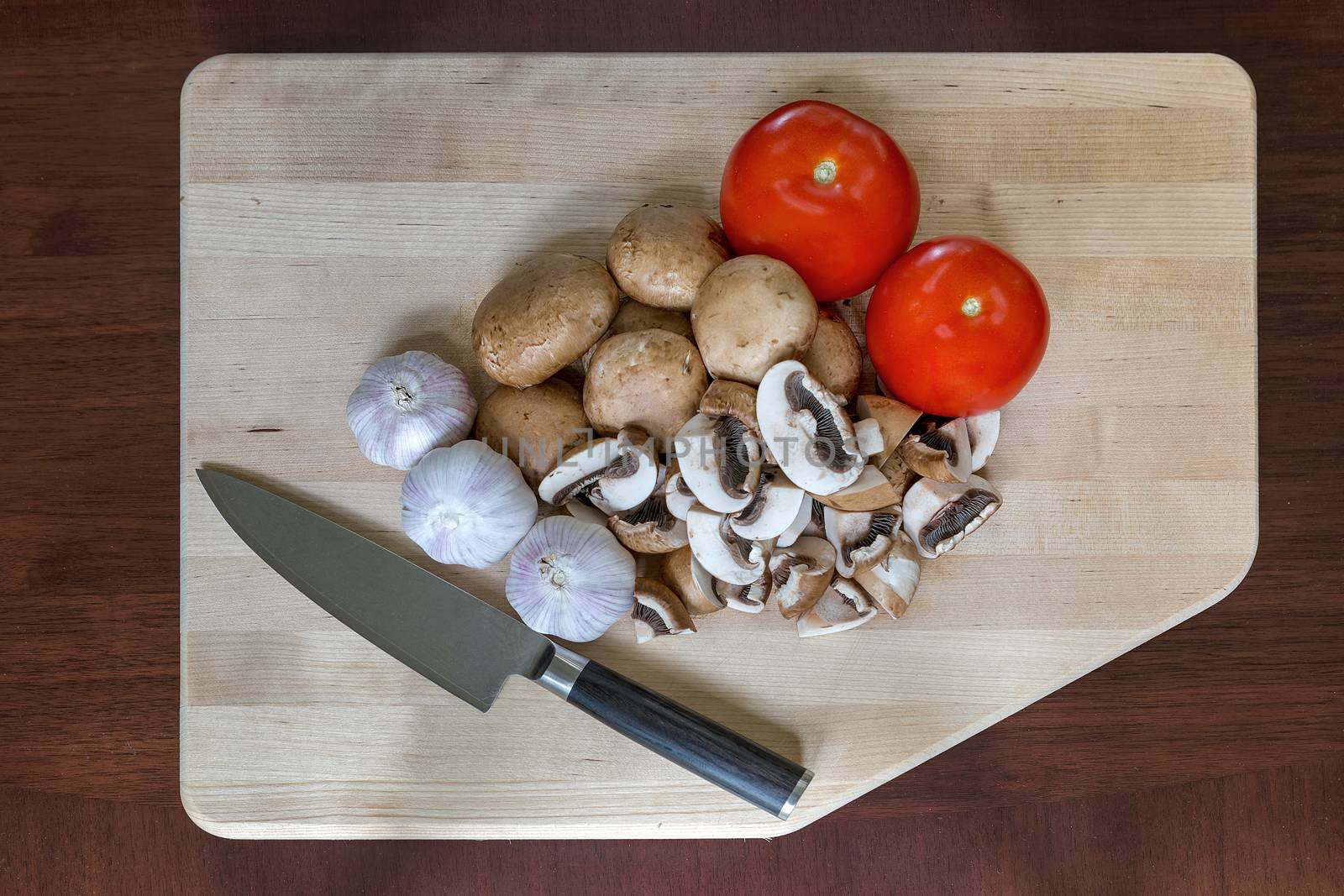 Mushrooms tomatoes garlic cloves vegetable with kitchen knife on wood cutting board