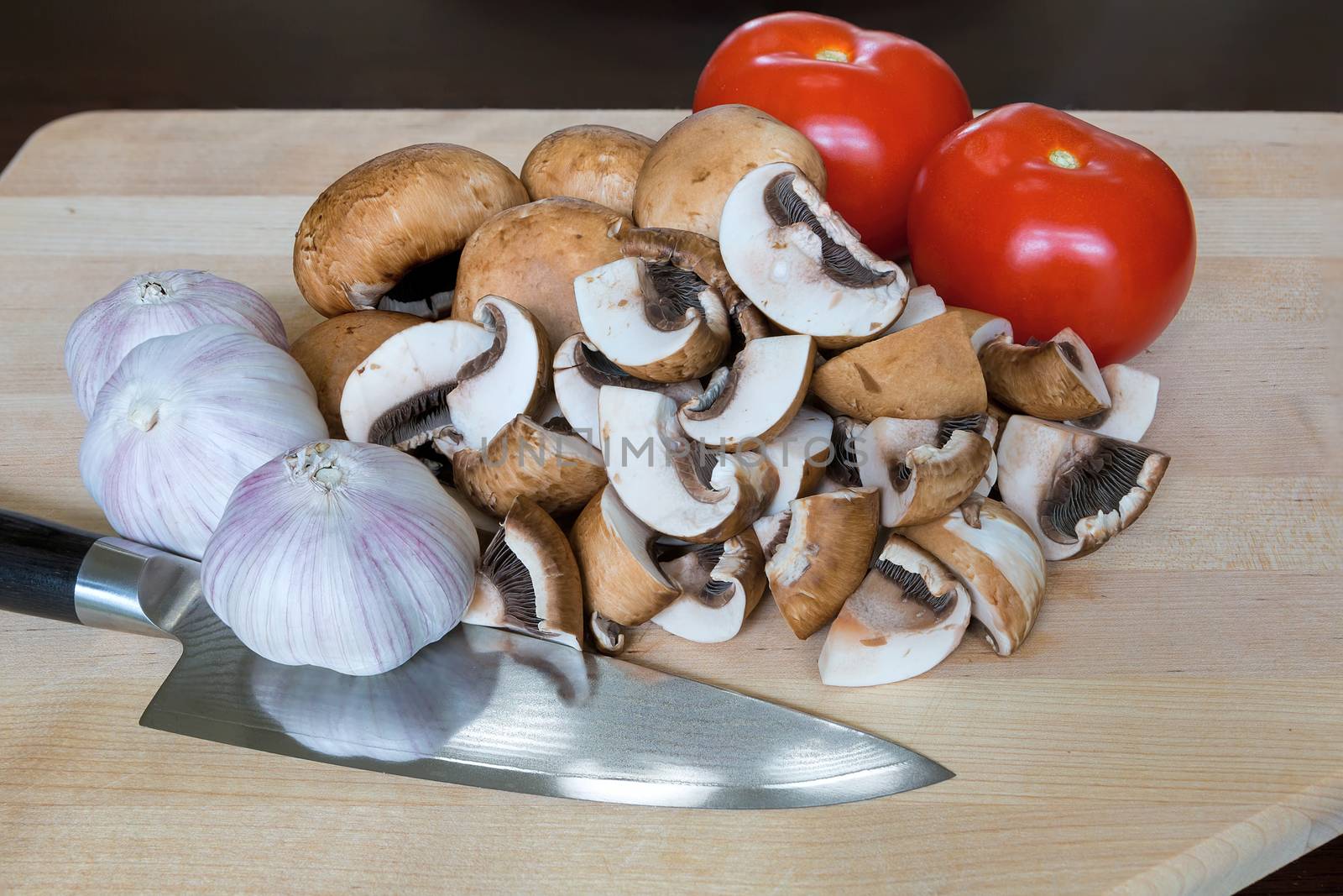 Portobello mushrooms tomatoes garlic cloves vegetable with kitchen knife on wood cutting board closeup
