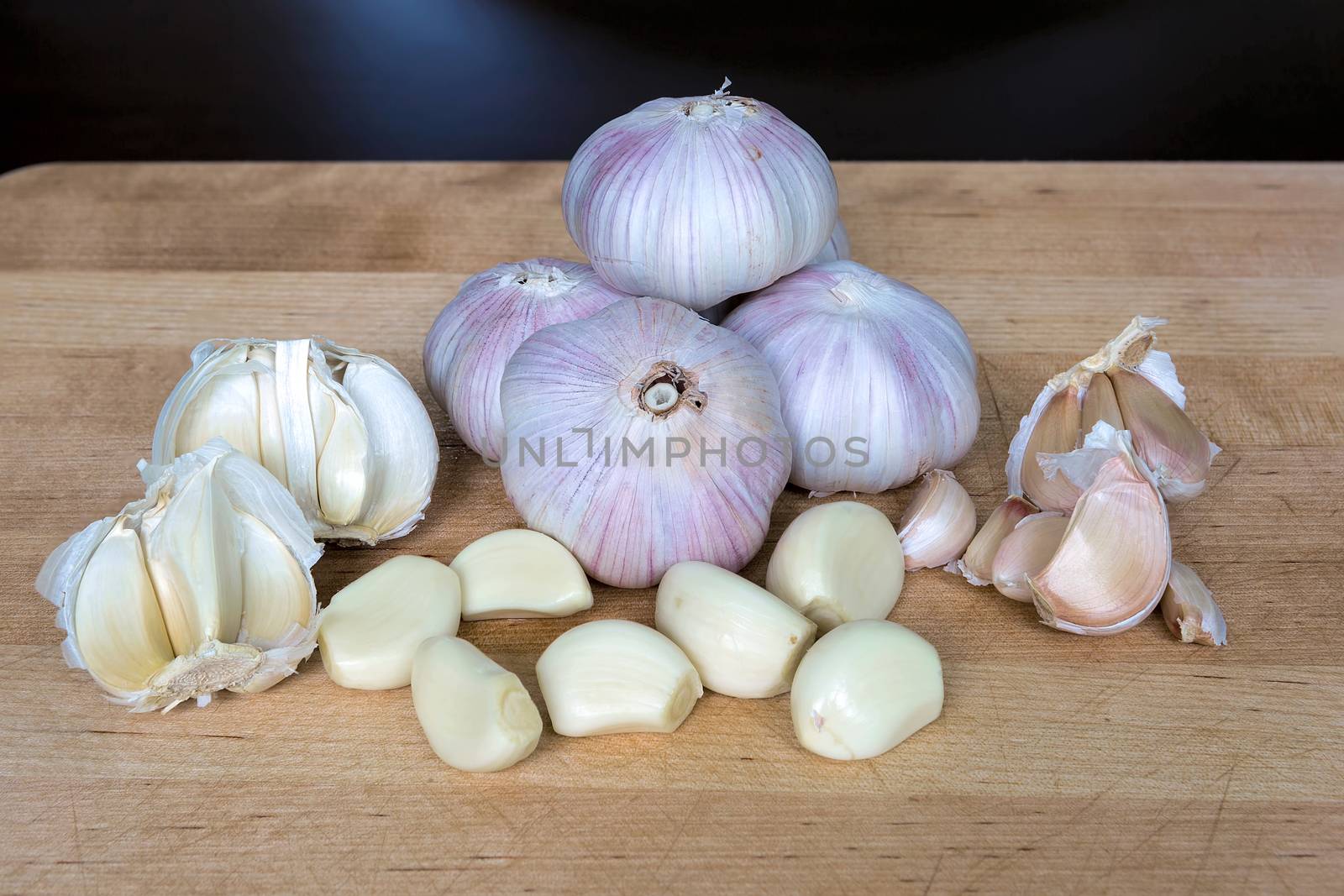 Whole and peeled garlic cloves on kitchen wood cutting board closeup macro