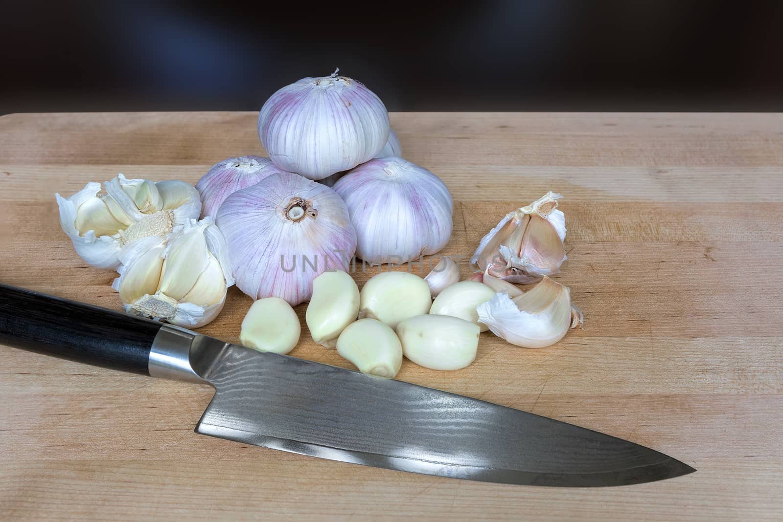 Whole and peeled garlic cloves kitchen knife on kitchen wood cutting board closeup macro