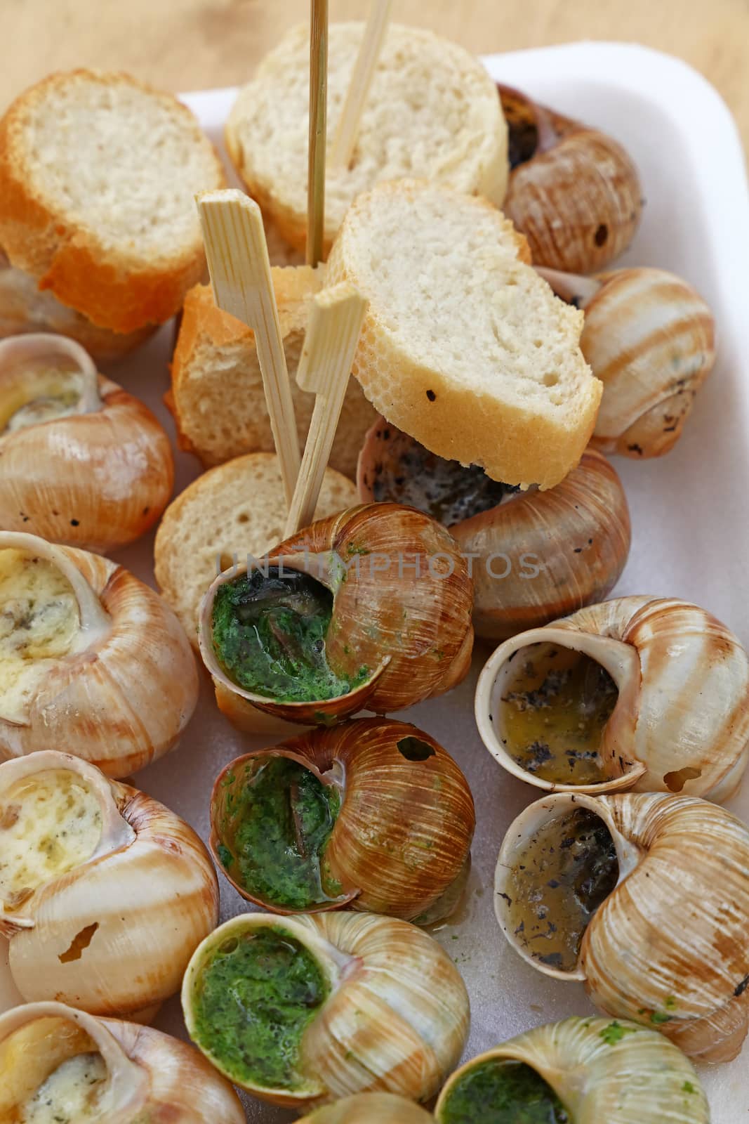 Close up street fast food take away portion of cooked escargot snails with French herbs and garlic butter and baguette bread, elevated top view, directly above