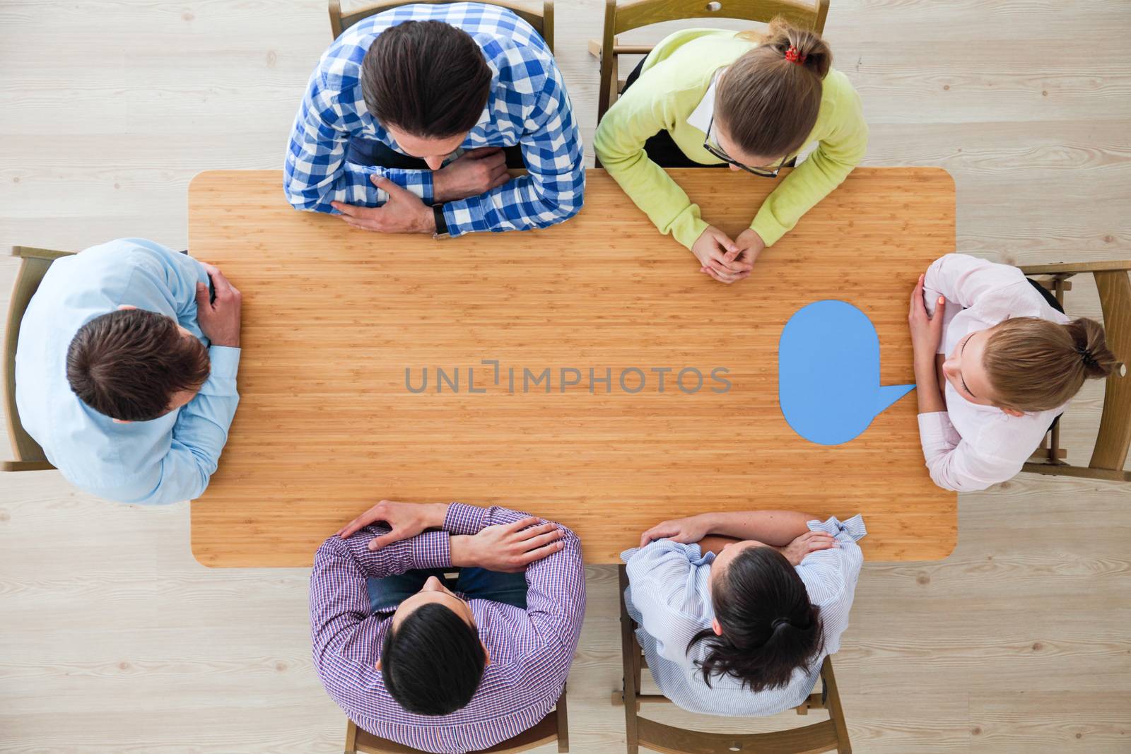 Team of business people in casual clothes sitting around the table with paper dialog boxes, discussing opinion concept
