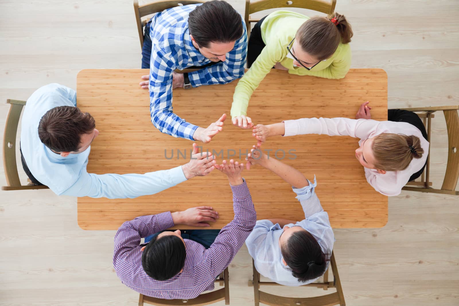 Coworkers doing high five sitting at the office table, top view