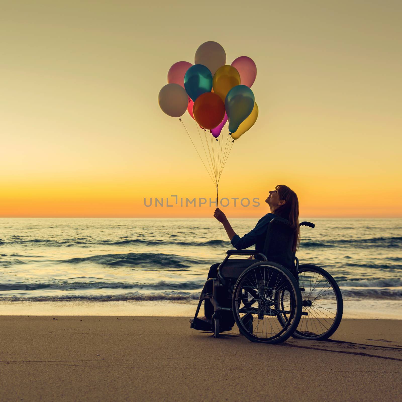 Handicapped woman on a wheelchair with colored balloons at the beach