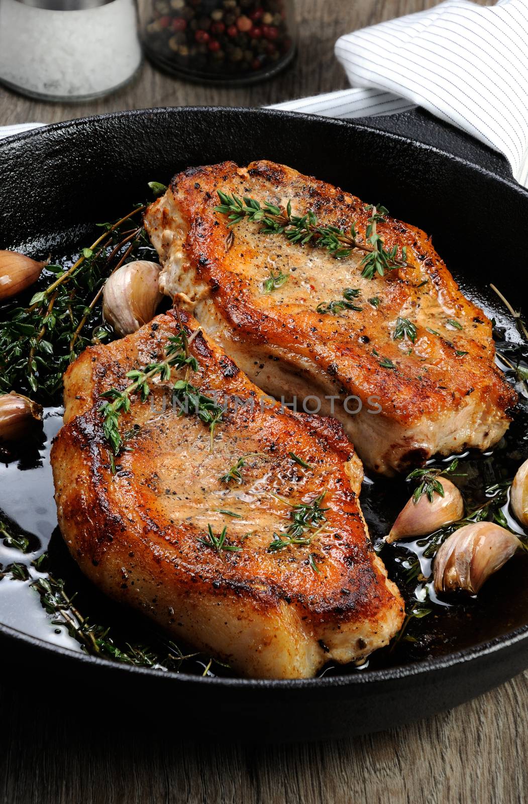 Juicy, browned pork steak on a bone in oil with garlic and herbs in a frying pan.