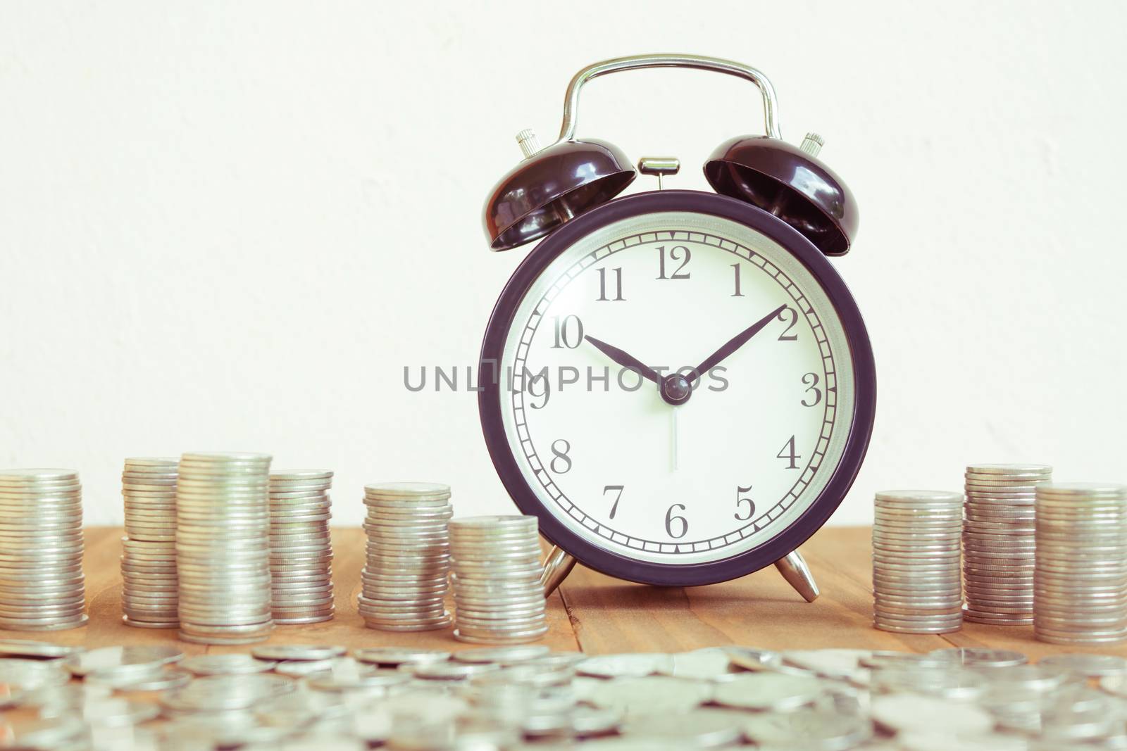 Stack of coins with black fashioned alarm clock for display planning money financial and business accounting concept, time is money concept with clock and coins, time to work at make money, vintage color tone by rakoptonLPN